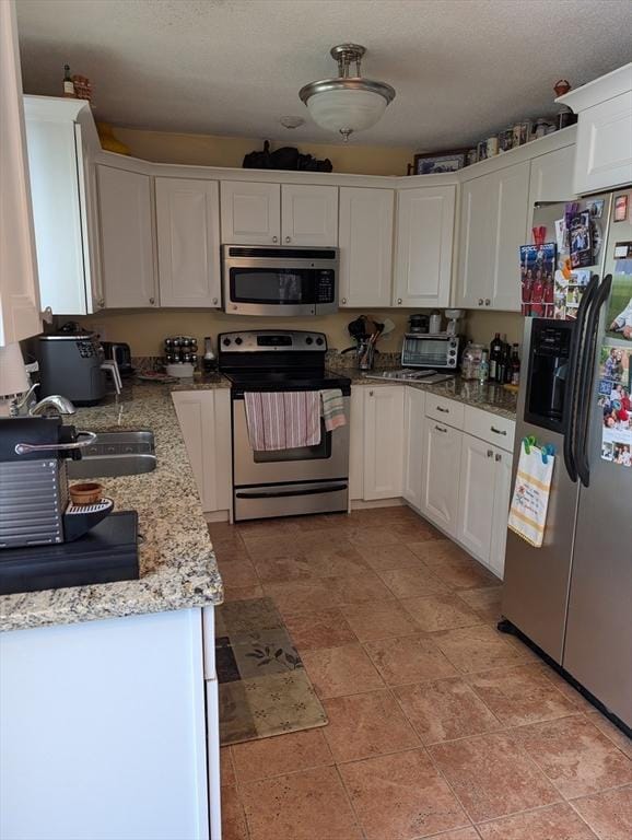 kitchen featuring appliances with stainless steel finishes, sink, white cabinets, light stone counters, and a textured ceiling