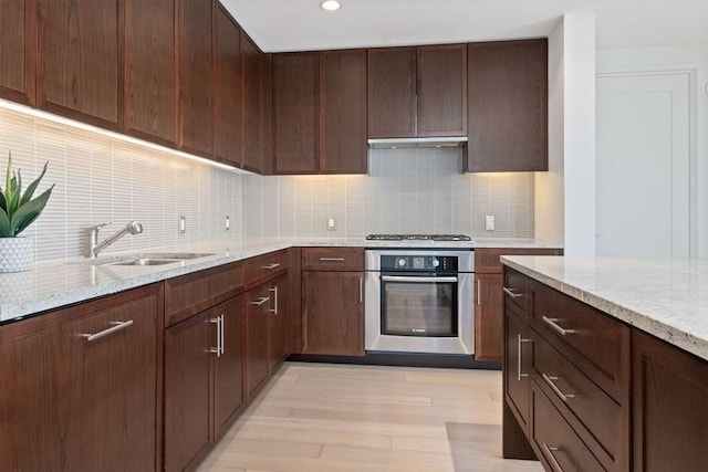 kitchen featuring dark brown cabinets, stainless steel appliances, light stone countertops, extractor fan, and sink