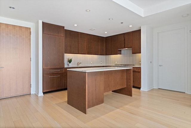 kitchen with stainless steel gas stovetop, a kitchen island, light wood-type flooring, and backsplash