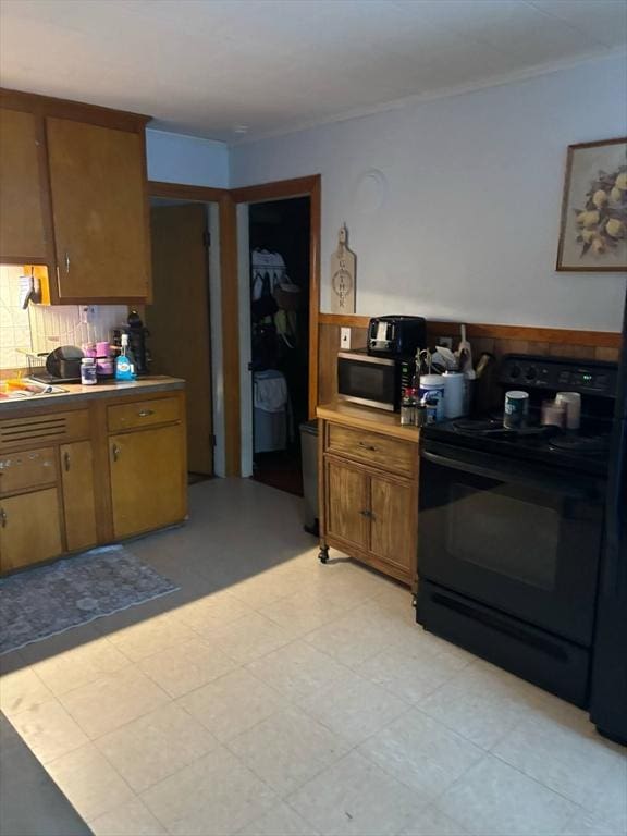 12 Woodmont St, Westfield, MA 01085 - kitchen with black electric range oven, stainless steel microwave, ornamental molding, brown cabinets, and tasteful backsplash
