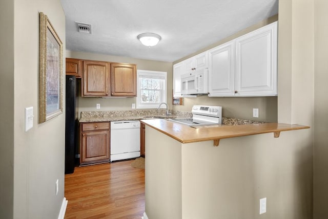 kitchen with sink, a kitchen breakfast bar, white appliances, kitchen peninsula, and light wood-type flooring