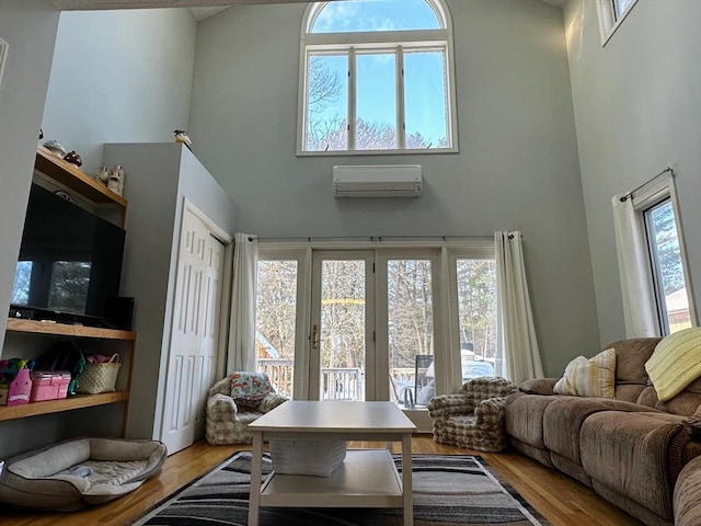 living room featuring an AC wall unit, a healthy amount of sunlight, a towering ceiling, and wood finished floors