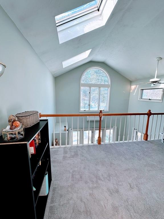 interior space featuring a ceiling fan, lofted ceiling with skylight, and carpet