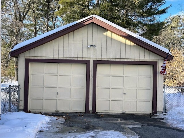 snow covered garage featuring fence and a detached garage