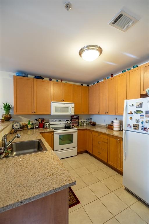 kitchen with light tile patterned flooring, light stone counters, white appliances, and sink