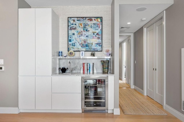bar featuring light wood-style floors, a sink, baseboards, indoor wet bar, and wine cooler