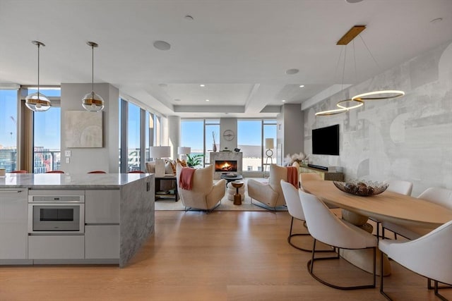 kitchen featuring light wood-style floors, open floor plan, pendant lighting, and a warm lit fireplace