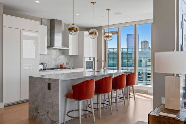 kitchen with light wood-style flooring, wall chimney exhaust hood, modern cabinets, and white cabinets