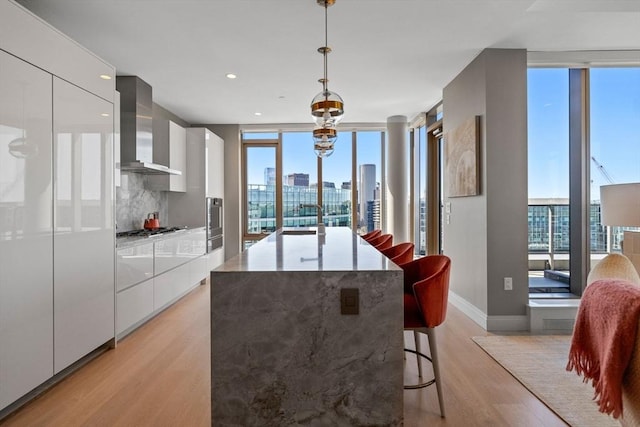 kitchen with wall chimney range hood, a healthy amount of sunlight, modern cabinets, light wood finished floors, and white cabinetry