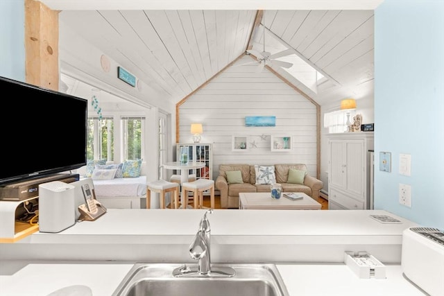 kitchen with sink, wood walls, wood ceiling, ceiling fan, and vaulted ceiling with skylight