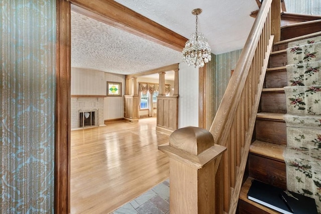 73 Biltmore St, Springfield, MA 01108 - stairway featuring a textured ceiling, a chandelier, wood finished floors, a fireplace, and decorative columns