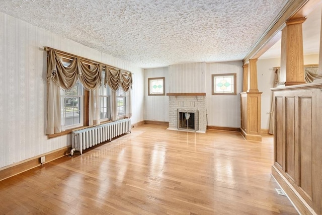 73 Biltmore St, Springfield, MA 01108 - unfurnished living room featuring radiator heating unit, light wood-style flooring, a fireplace, ornate columns, and wallpapered walls