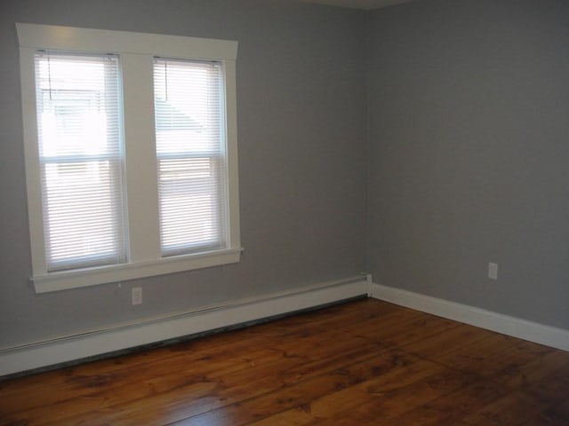 unfurnished room with dark wood finished floors, a baseboard heating unit, and baseboards