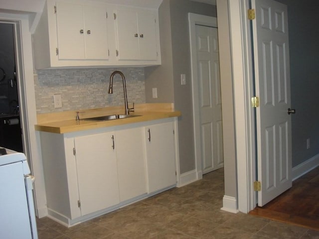 kitchen with a sink, backsplash, white cabinets, light countertops, and baseboards