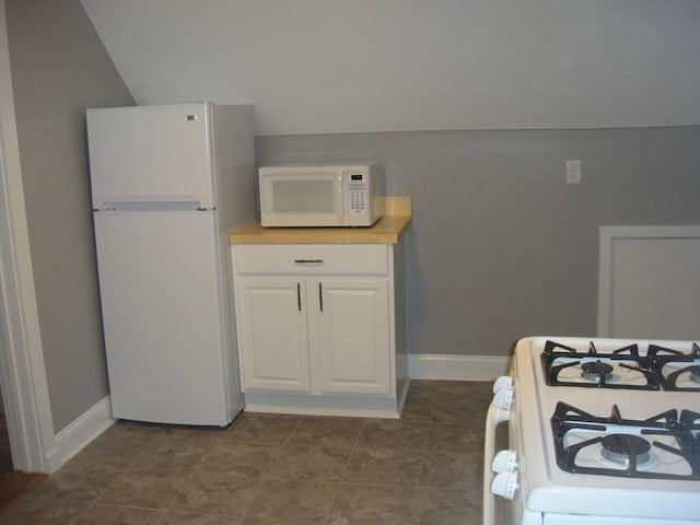 kitchen with white appliances, white cabinetry, baseboards, and vaulted ceiling