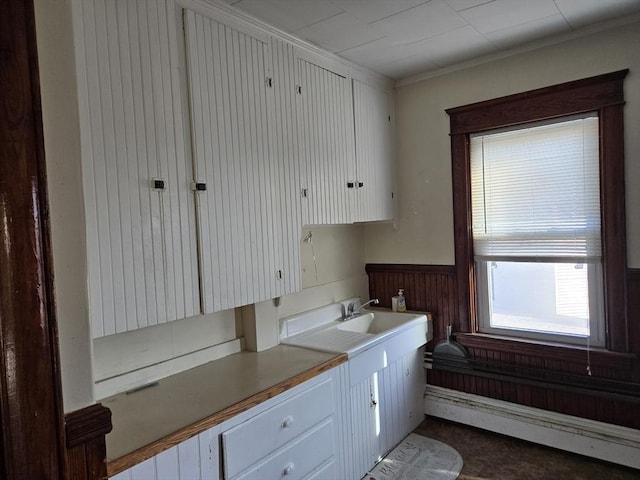 kitchen featuring white cabinetry, baseboard heating, wooden walls, and ornamental molding