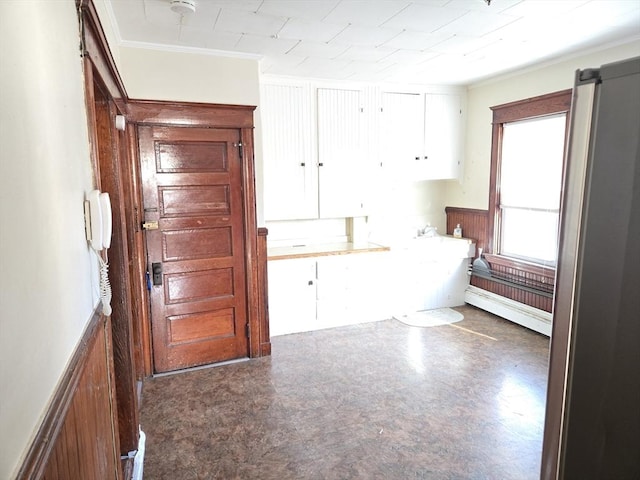 interior space with ornamental molding, a baseboard heating unit, and wood walls