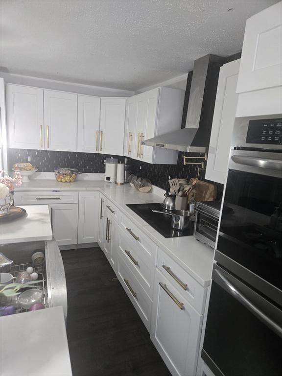 kitchen with wall chimney exhaust hood, a textured ceiling, black electric cooktop, double oven, and white cabinetry