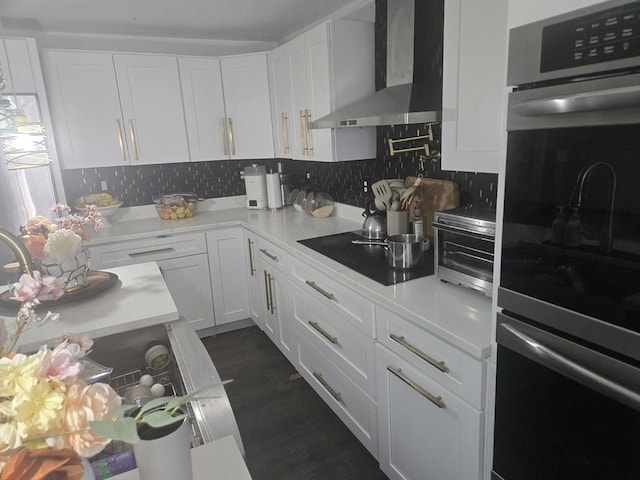 kitchen featuring white cabinets, decorative backsplash, wall chimney range hood, and double oven