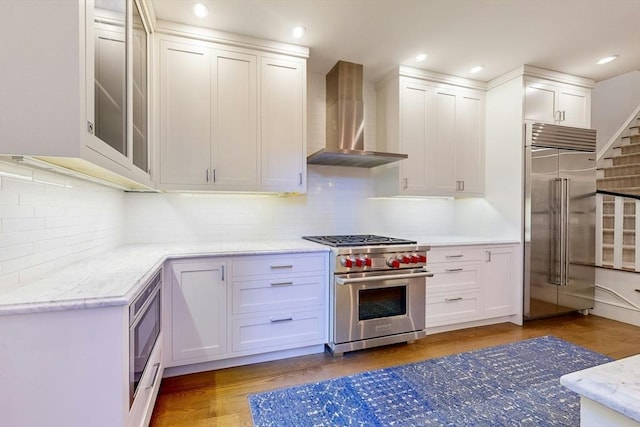 kitchen featuring built in appliances, white cabinetry, wall chimney exhaust hood, and hardwood / wood-style flooring