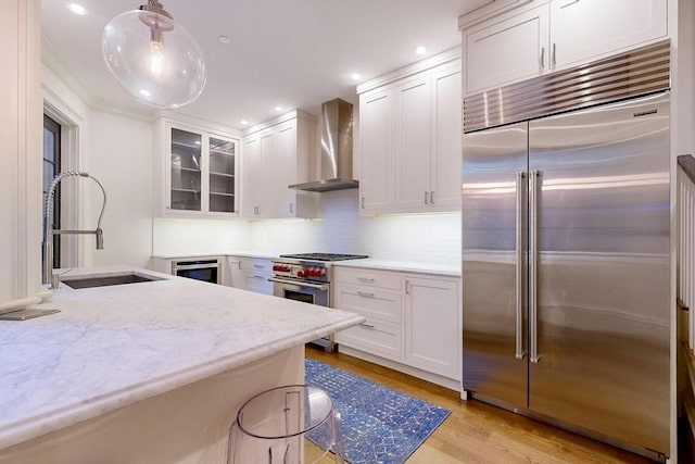 kitchen with white cabinetry, sink, wall chimney range hood, premium appliances, and pendant lighting