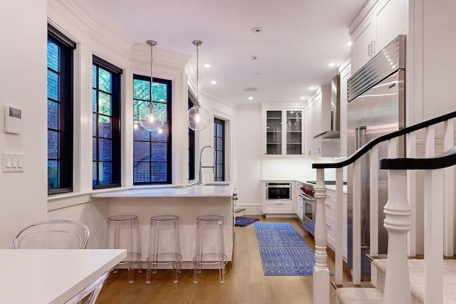 interior space featuring sink, decorative light fixtures, premium appliances, light hardwood / wood-style floors, and white cabinetry