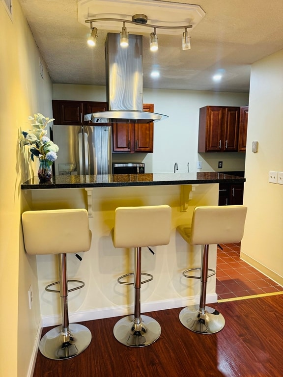 kitchen with stainless steel refrigerator, island exhaust hood, dark hardwood / wood-style flooring, a kitchen breakfast bar, and a textured ceiling