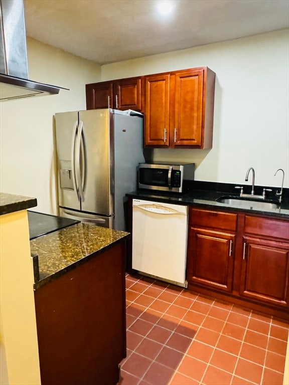 kitchen with dark stone countertops, sink, extractor fan, tile patterned flooring, and appliances with stainless steel finishes