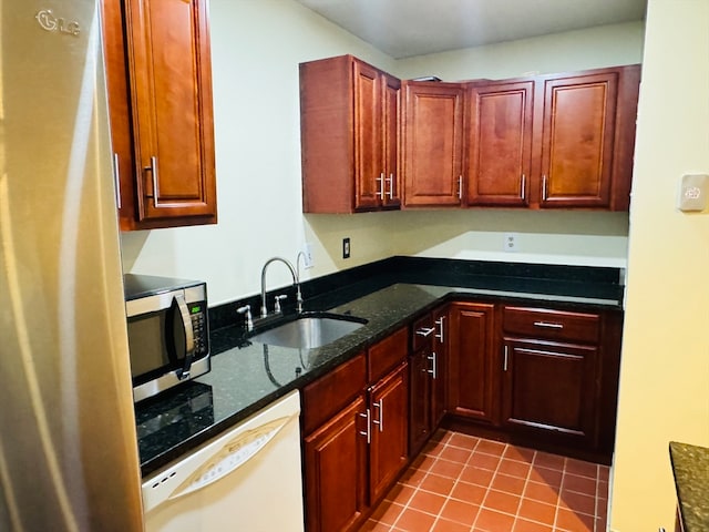 kitchen with light tile patterned floors, dark stone countertops, sink, and stainless steel appliances