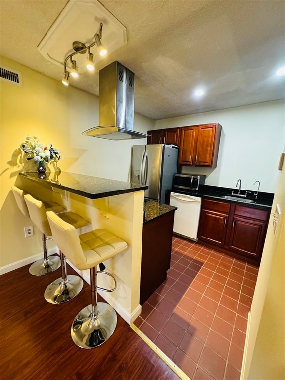 kitchen with dark tile patterned flooring, sink, extractor fan, appliances with stainless steel finishes, and a breakfast bar