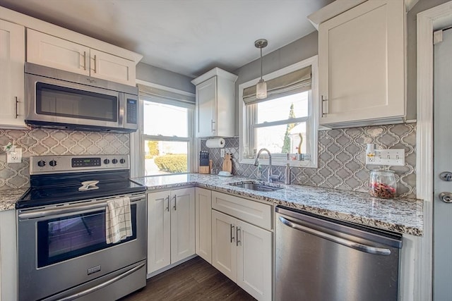 kitchen with light stone countertops, appliances with stainless steel finishes, sink, pendant lighting, and white cabinets