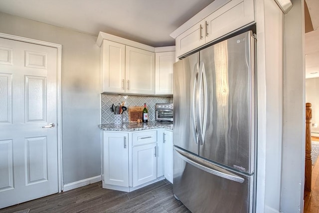 kitchen with light stone counters, white cabinetry, dark wood-type flooring, and stainless steel refrigerator