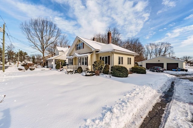 snow covered property with a garage, a chimney, and an outbuilding