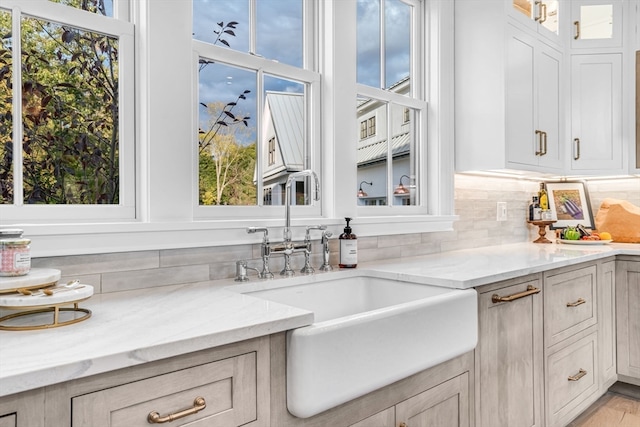 kitchen featuring light wood-type flooring, light stone counters, sink, and tasteful backsplash