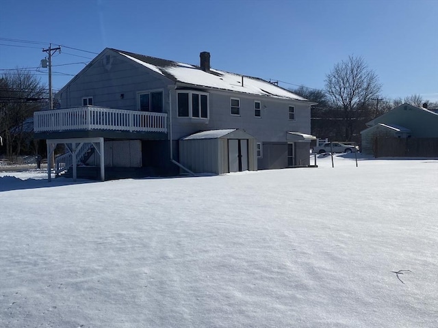 snow covered house featuring a deck and a shed