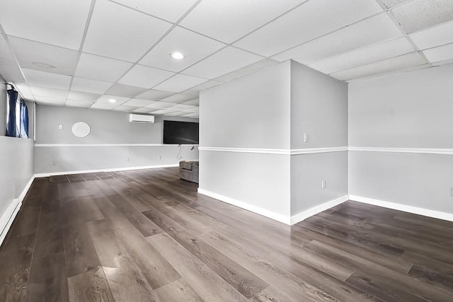 finished below grade area with a drop ceiling, wood finished floors, a wall mounted AC, baseboards, and recessed lighting