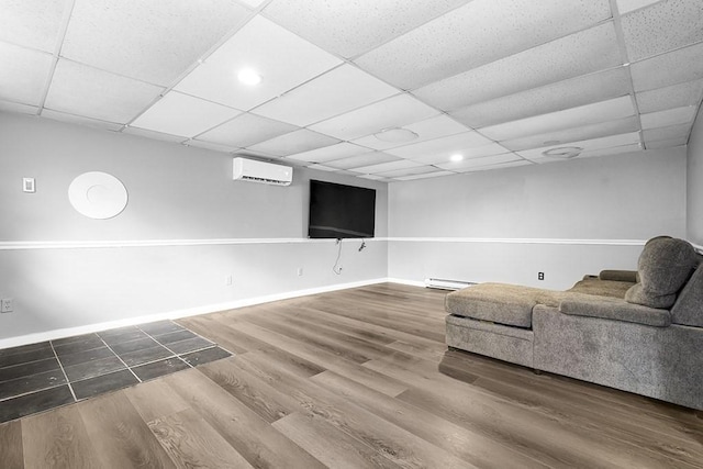 living room with an AC wall unit, baseboard heating, wood finished floors, a paneled ceiling, and baseboards