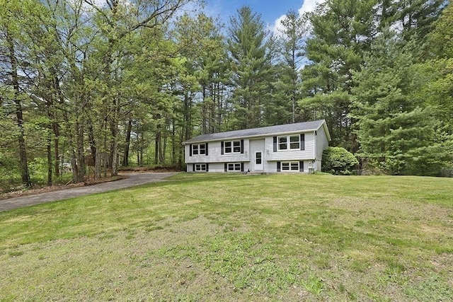 bi-level home featuring a front lawn, driveway, and a forest view