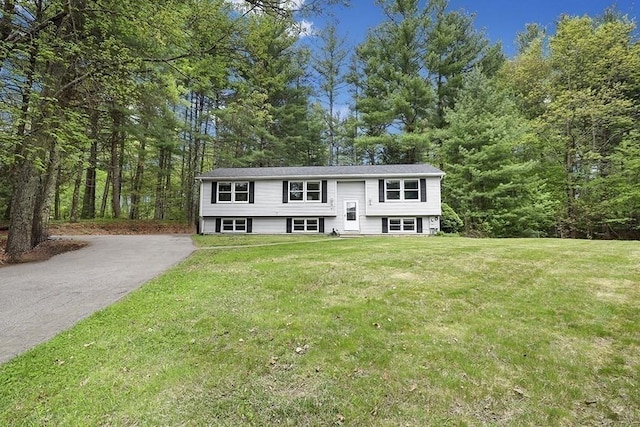 split foyer home with a front lawn, a wooded view, and driveway