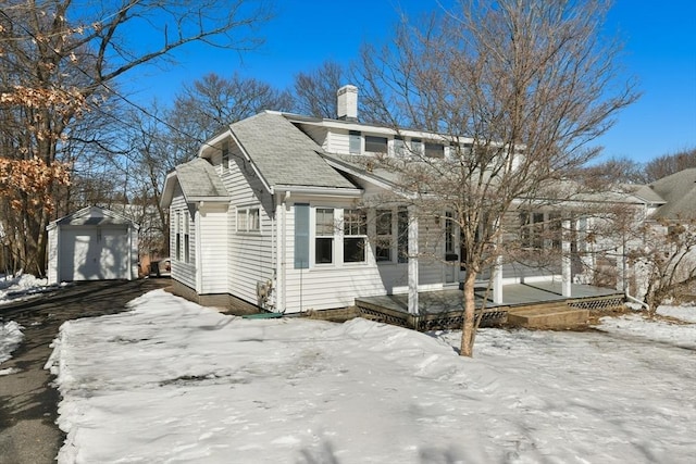 view of front facade with a garage, a shingled roof, an outdoor structure, a shed, and a chimney