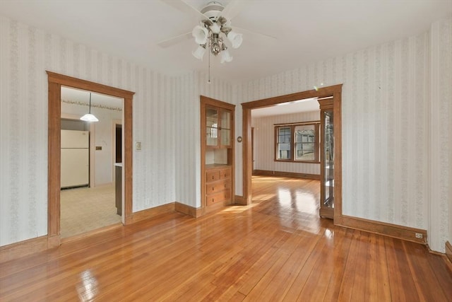 unfurnished room with ceiling fan, light wood-style flooring, baseboards, and wallpapered walls