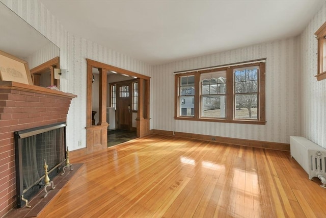 unfurnished living room featuring a fireplace, baseboards, radiator heating unit, wood-type flooring, and wallpapered walls