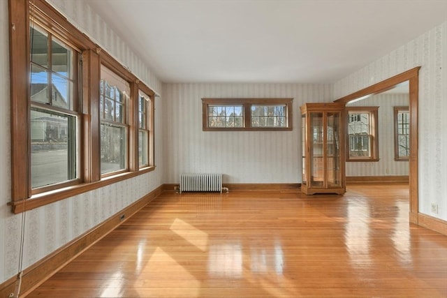 spare room featuring wallpapered walls, radiator heating unit, baseboards, and light wood-style flooring