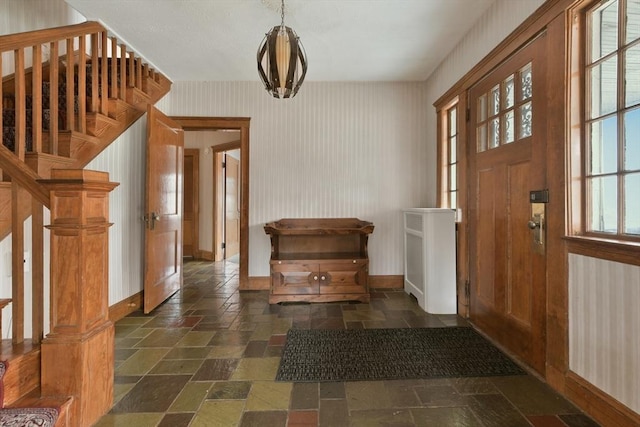 foyer entrance featuring stairs, baseboards, and stone tile floors