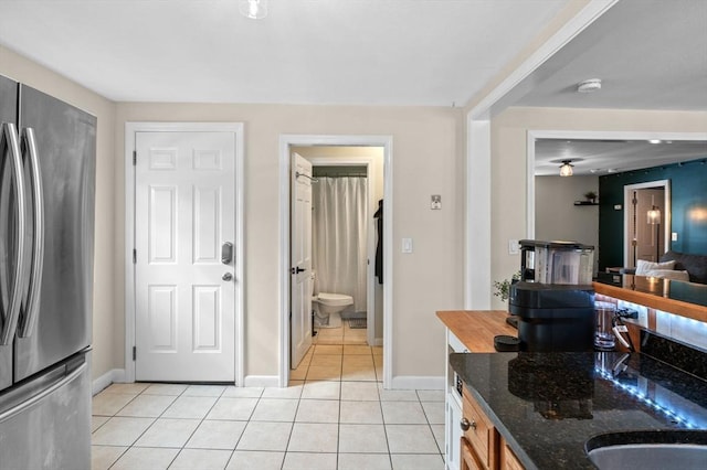 kitchen featuring freestanding refrigerator, baseboards, dark stone countertops, and light tile patterned floors