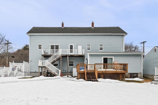 snow covered house with stairway and a wooden deck