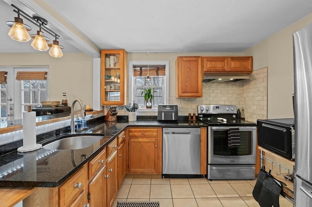 kitchen with light tile patterned floors, under cabinet range hood, a sink, appliances with stainless steel finishes, and tasteful backsplash