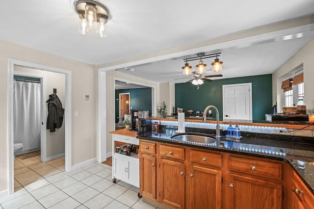 kitchen featuring light tile patterned floors, dark stone counters, brown cabinetry, hanging light fixtures, and a sink