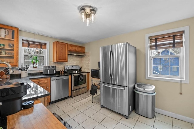 kitchen featuring light tile patterned flooring, under cabinet range hood, stainless steel appliances, a sink, and backsplash