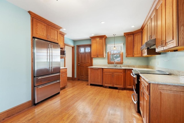 kitchen with pendant lighting, sink, light stone counters, stainless steel appliances, and light hardwood / wood-style flooring